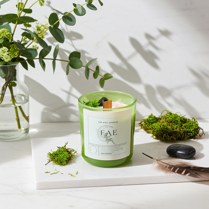 Green candle labeled 'FAE' on a white surface with plants and stones