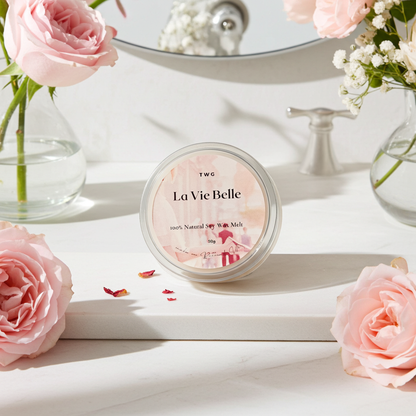 TWG La Vie Belle candle on a white surface with pink roses and a mirror in the background